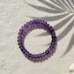 Purple beaded bracelet on a light surface with a leaf shadow